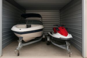 A speed boat and a jet ski are parked inside a self-storage unit.